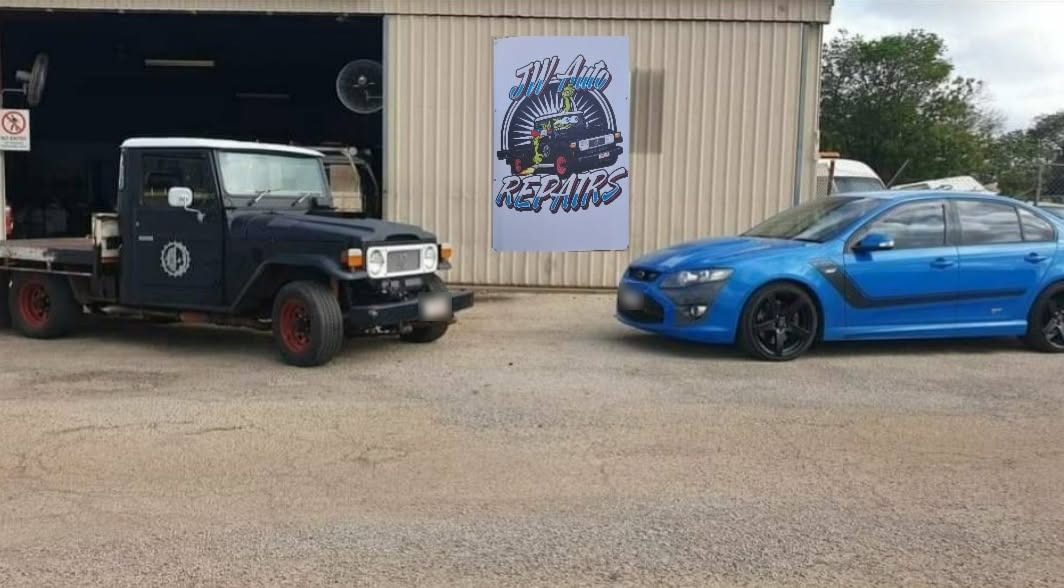 The JW Auto Repairs workshop shed on Pearce Street, with the logo sign on the wall, the navy LandCruiser tray-back out front and a blue sedan